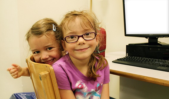 2 young girls smiling in front of a computer