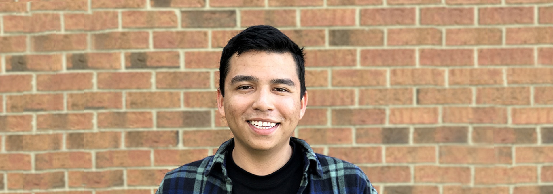 Josh Lopez standing in front of a brick wall smiling