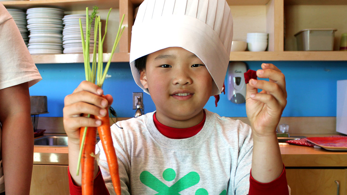Young boy wearing a chef's hat holding a carrot
