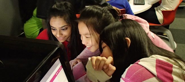 3 young girls laughing together while staring at a computer screen